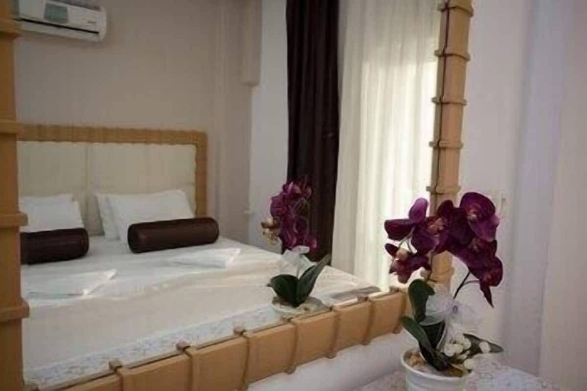 A hotel room with a bed, a window with curtains, and a potted orchid plant.