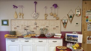 A breakfast buffet setup with various food items, a coffee-themed wall decoration, and a calendar on the wall. - Albergo Trattoria Italia (Desenzano del Garda)