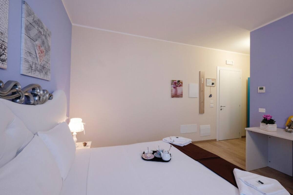 Une chambre d’hôtel avec un lit, une table de chevet, une lampe et un petit bureau agrémenté d’une plante.