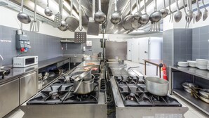 A commercial kitchen with stainless steel appliances, hanging utensils, and a microwave. - Albergo Trattoria Italia (Desenzano del Garda)