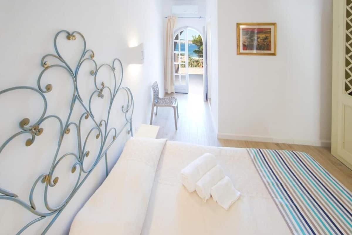 A bedroom with a metal headboard, a bed with white linens, a striped rug, and a view of a balcony.