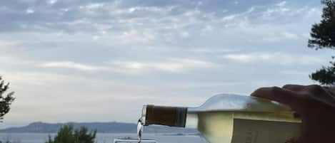 Une personne verse du vin blanc dans un verre, avec en arrière-plan une vue panoramique sur une étendue d’eau et des bâtiments.
