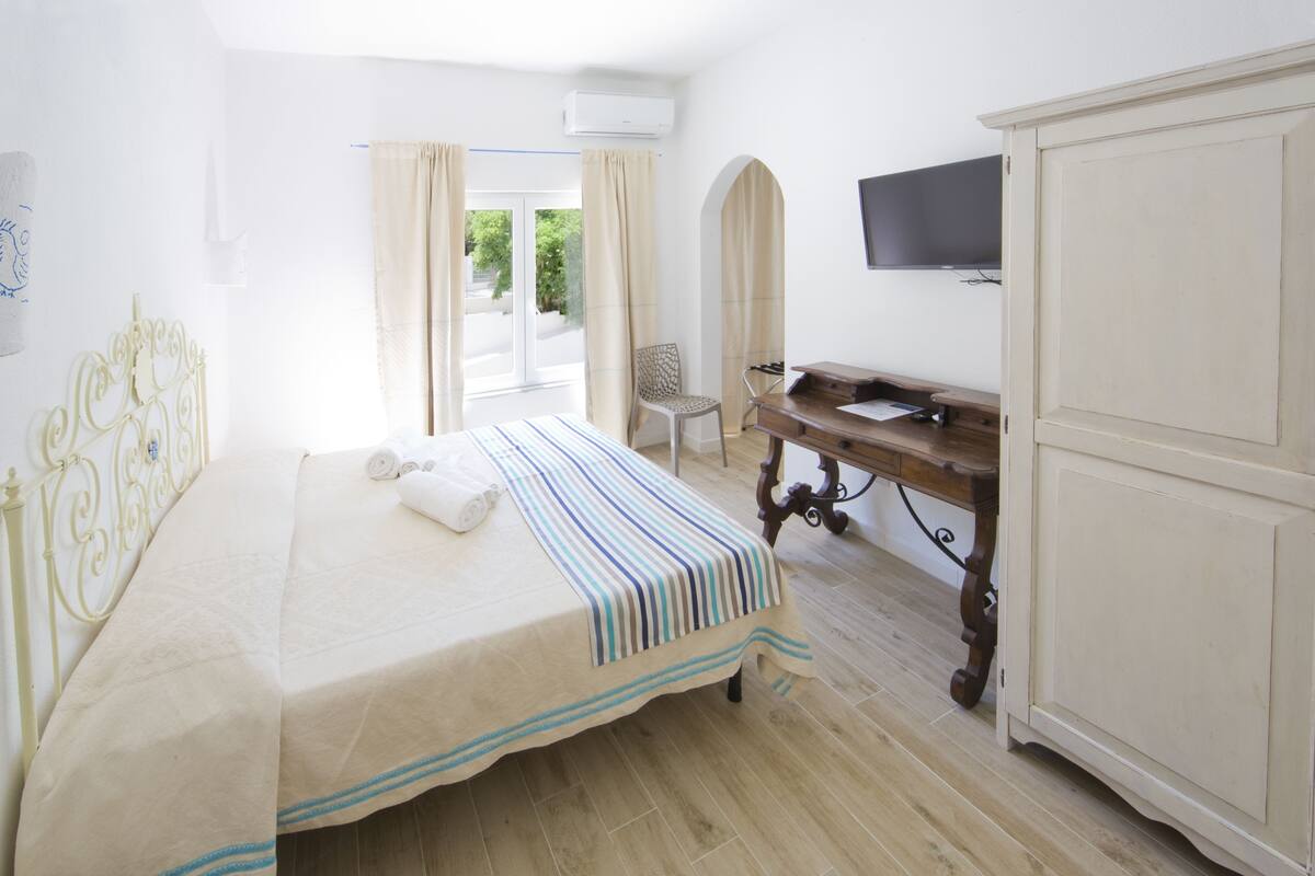 A bedroom with a bed, a desk, a chair, and a TV on the wall.