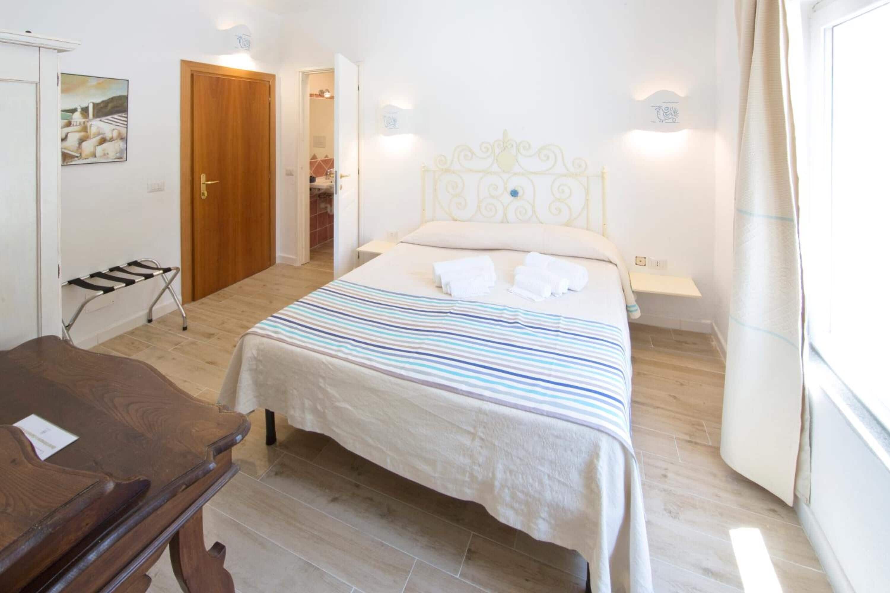Un dormitorio con una cama, un escritorio de madera, una puerta y una lámpara fijada a la pared.