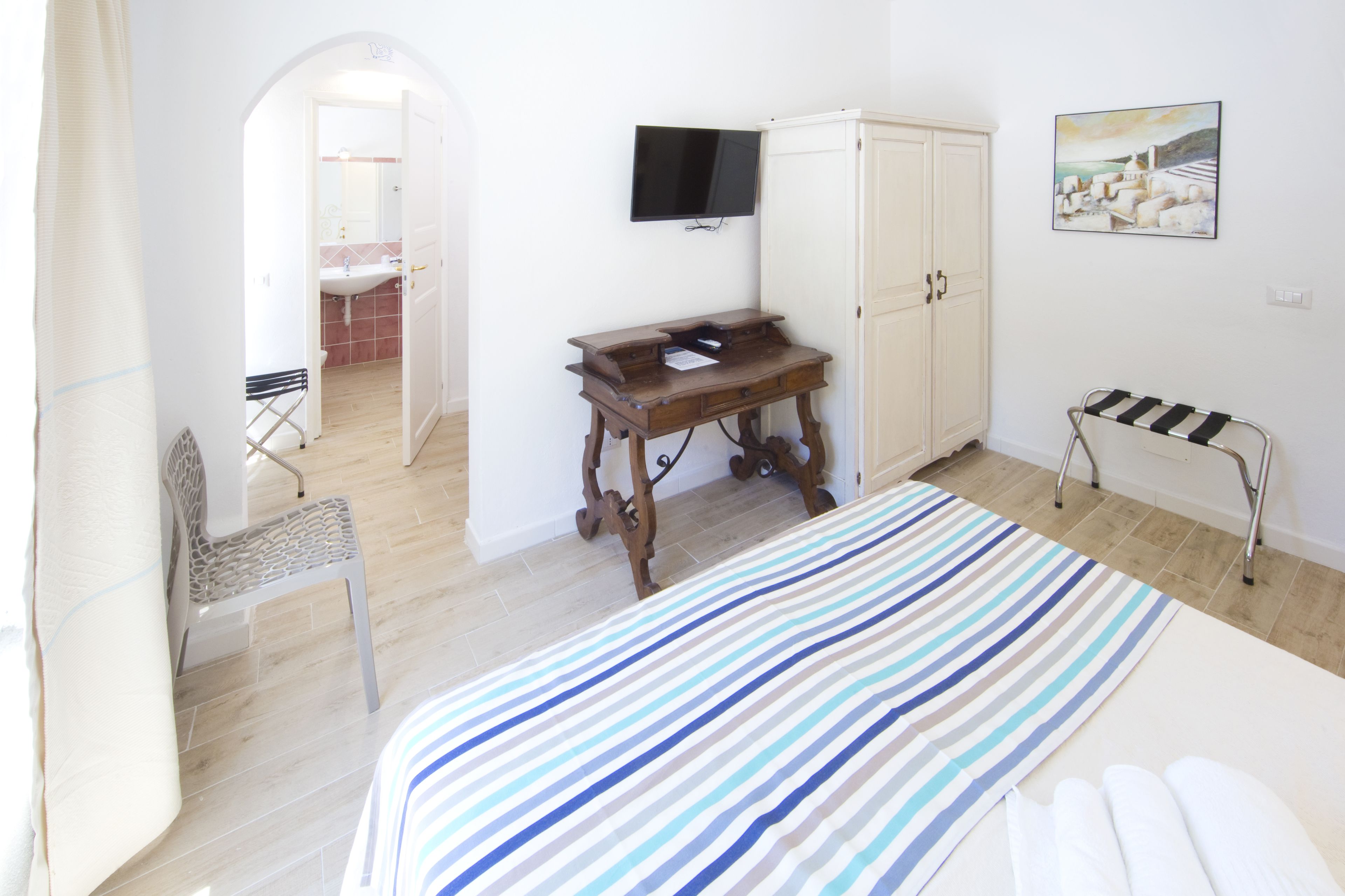 Un dormitorio con cama, escritorio, silla, armario, televisor y un cuadro en la pared.
