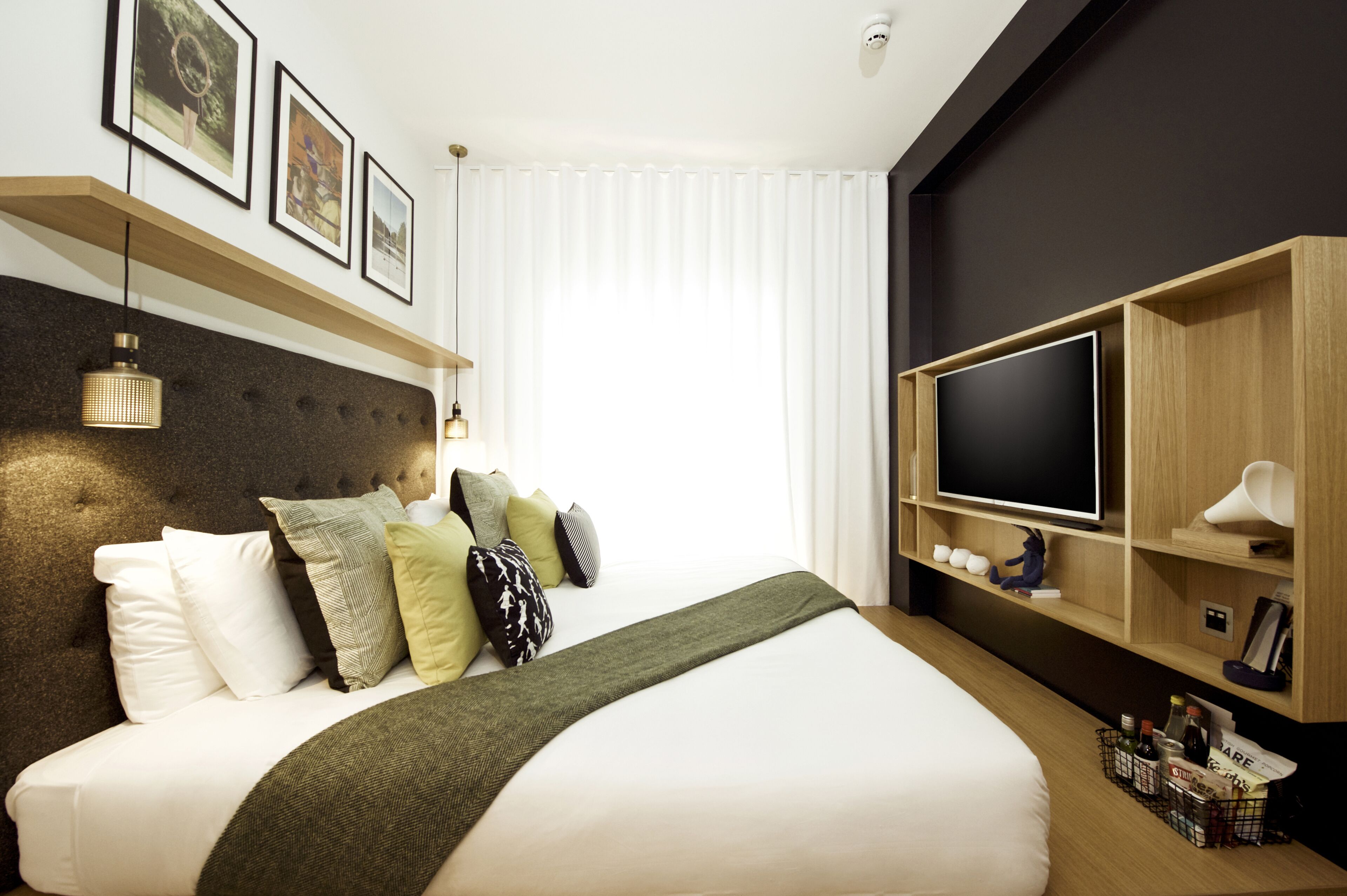 Een moderne hotelkamer met een groot bed, een flatscreentelevisie, houten planken en ingelijste foto’s aan de muur.