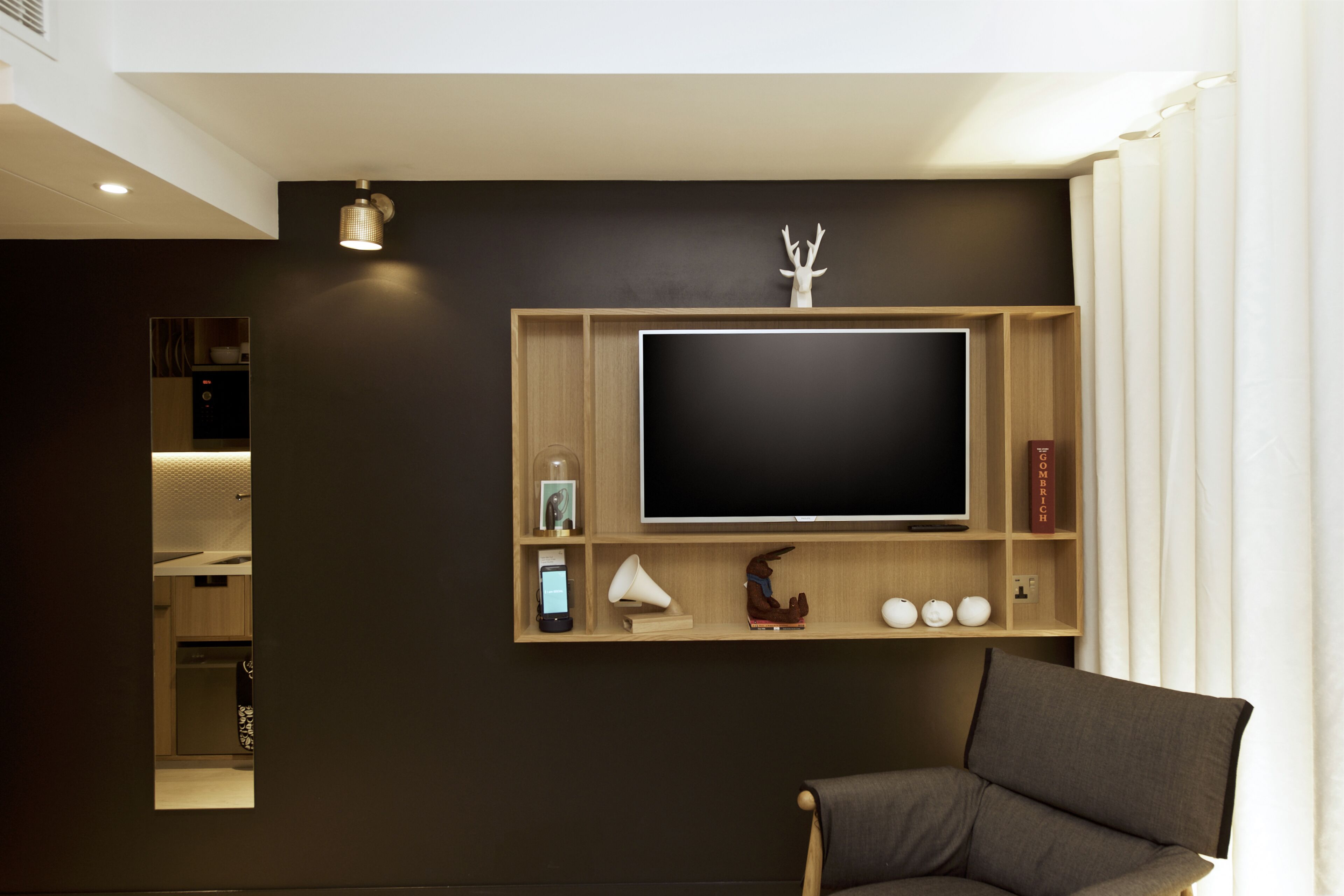 Un salon moderne doté d’un grand téléviseur à écran plat fixé sur un mur en bois, d’un fauteuil confortable et d’une petite étagère ornée d’objets décoratifs.