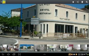 Un bâtiment portant l’inscription « LE MIDI BAR HOTEL RESTAURANT » et affichant un panneau indiquant les directions pour se rendre aux environs.