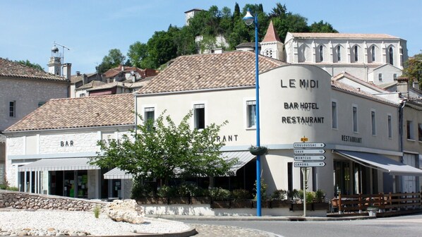 Un bâtiment portant l’inscription « LE MDI BAR HOTEL RESTAURANT » et affichant une signalétique indiquant les distances vers les lieux d’intérêt à proximité.
