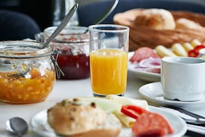 A breakfast table with a glass of orange juice, a jar of jam, a plate with bread, cheese, and tomatoes, and a white cup. - Danhostel Rebild (Skorping)