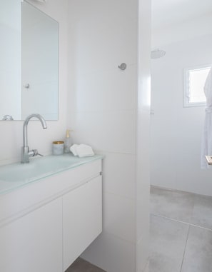 A modern bathroom with a glass sink, a large mirror, a shower, and a window.
