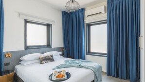 A modern hotel room with a large bed, two windows, an air conditioning unit, and a breakfast tray on the bed.