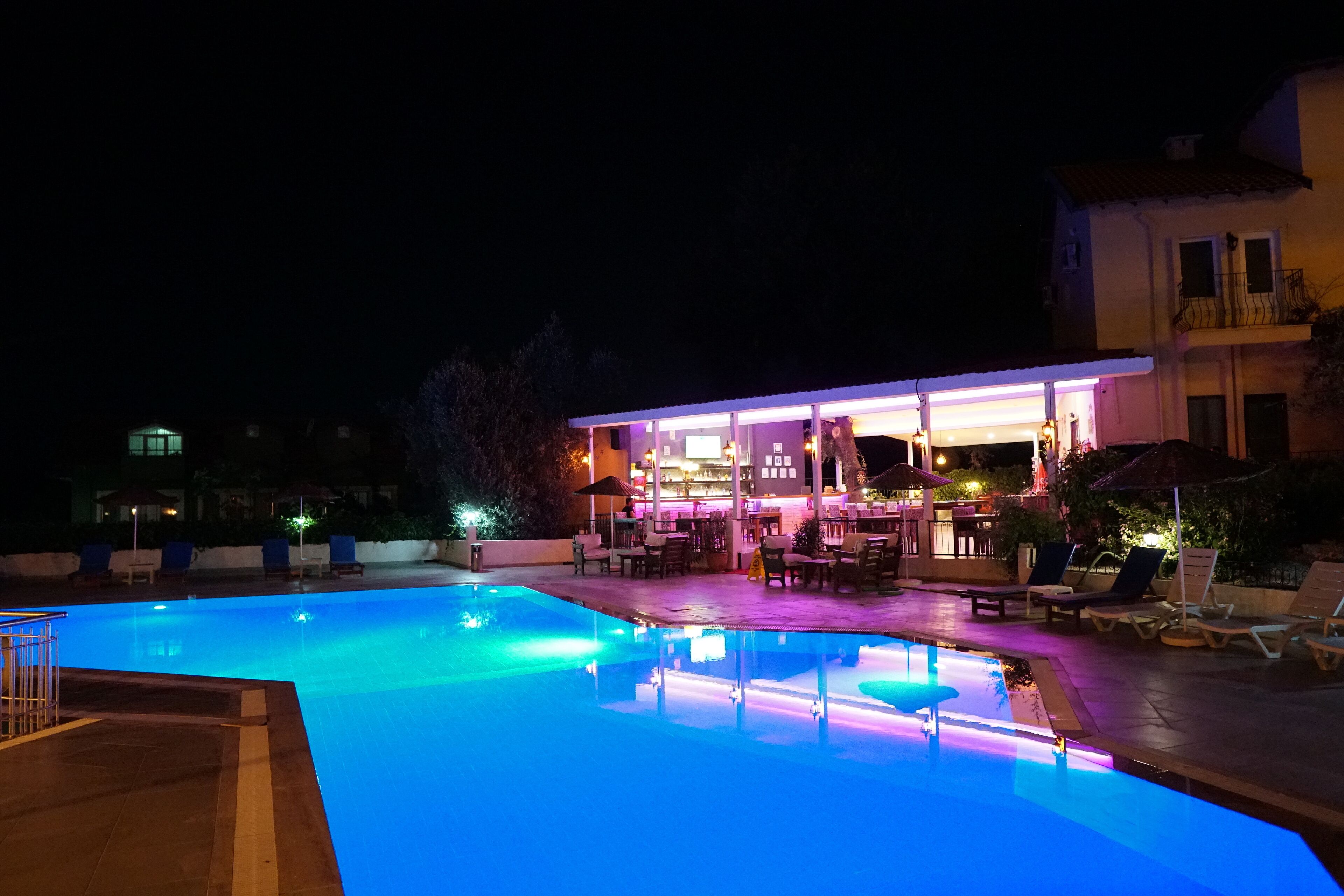 Area piscina illuminata di notte, con bar e poltrone relax.