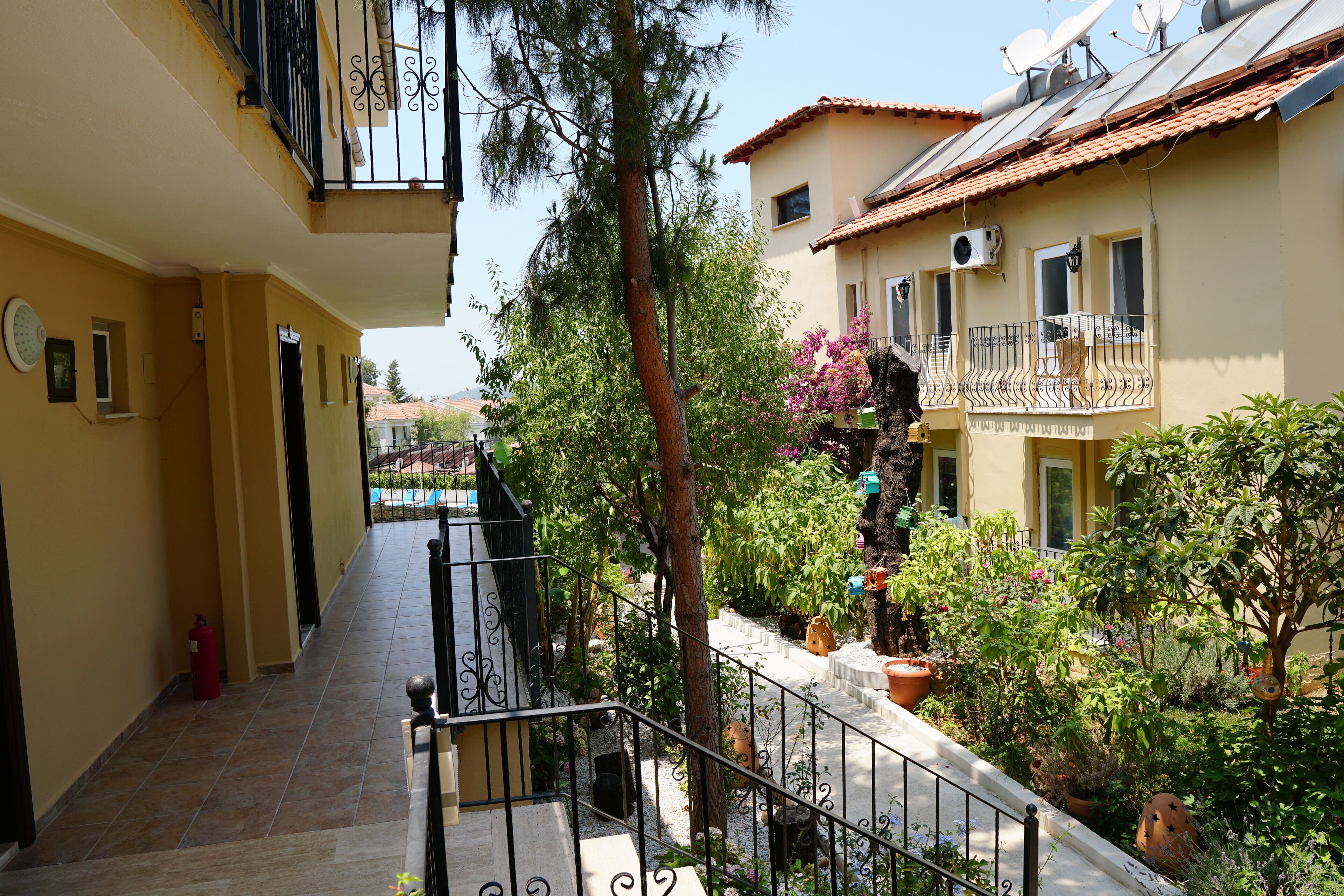 Um edifício residencial com varanda, escadaria e um jardim com plantas em vasos.