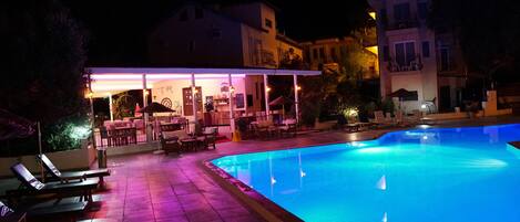 A swimming pool with lounge chairs and a covered seating area with tables and chairs.