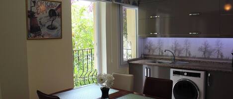 Cocina compacta con lavadora integrada, una mesa de comedor con sillas y ventana con vistas a zonas verdes.