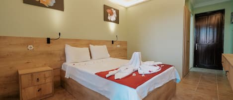Una cama bien hecha con un edredón rojo, una mesita de noche de madera y dos cuadros colgados en la pared.