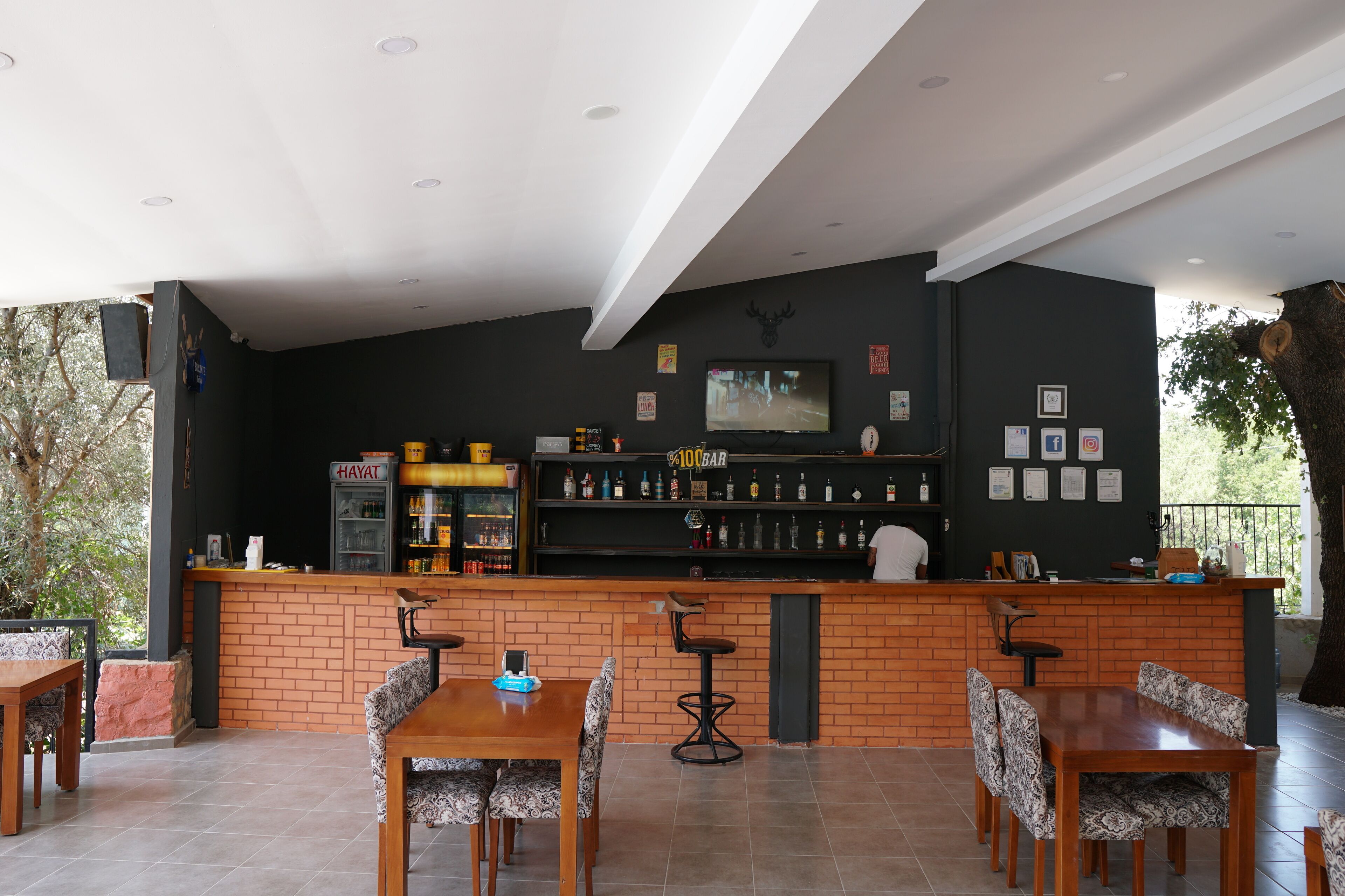 Zona de bar con mostrador de ladrillo, varias opciones de asientos, incluyendo una mesa de madera y sillas estampadas, y un televisor montado en la pared.