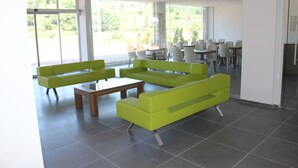 Un espacio interior moderno con asientos verdes, una mesa de centro de madera y ventanas amplias que ofrecen vistas al exterior.