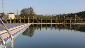 Una piscina con cubierta de madera y barandillas metálicas, rodeada de árboles y edificios al fondo.