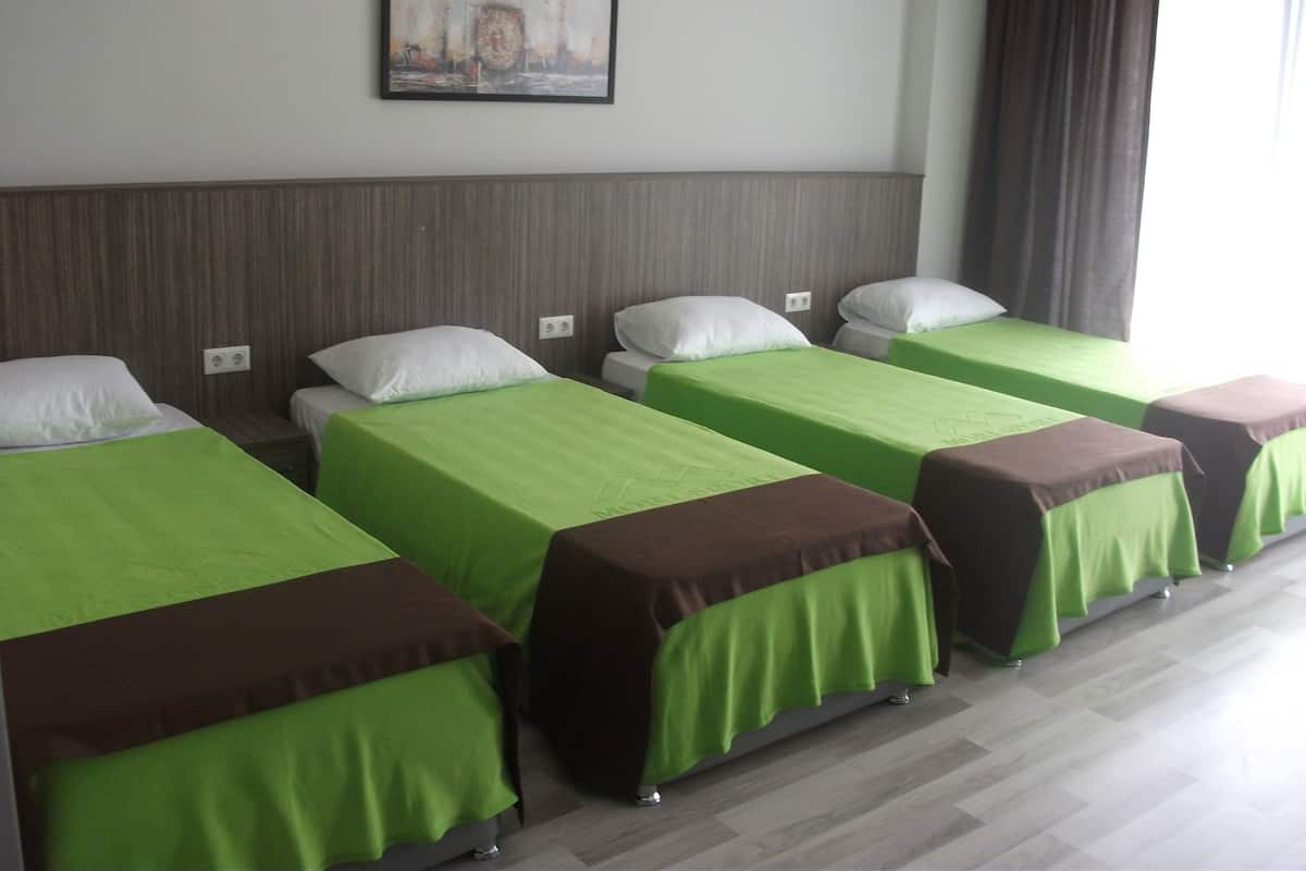 A hotel room with four single beds, each with a green bedspread and a brown headboard. There is a framed picture on the wall above the beds.