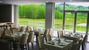 Un restaurante con mesas dispuestas para comer, amplios ventanales que ofrecen vistas a un paisaje verde.