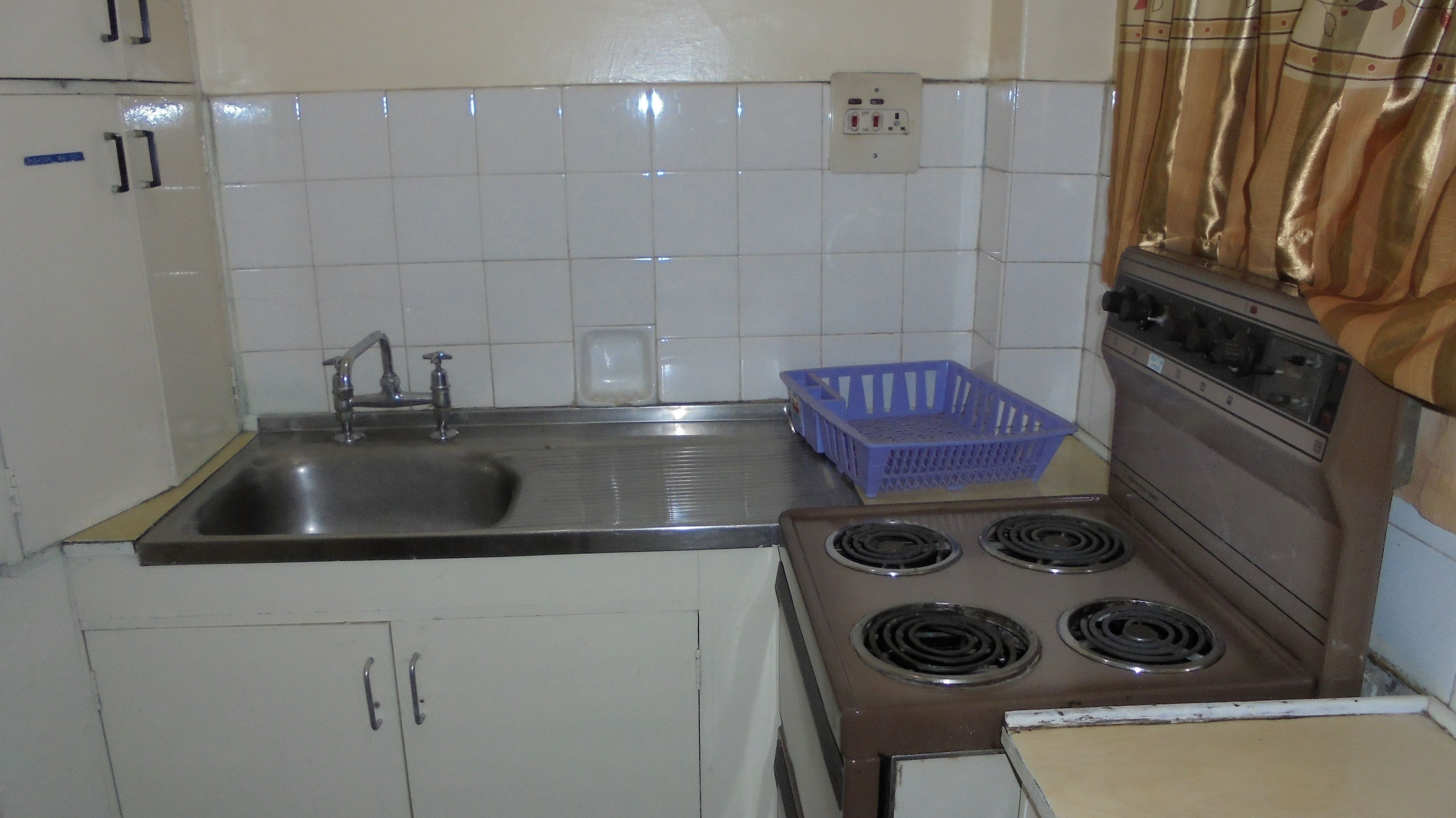 Una cocina con un lavamanos, estufa, armarios y una cesta azul.