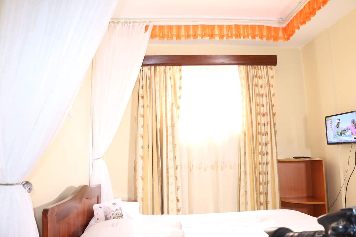A hotel room with a bed, curtains, a television, and a wooden shelf.