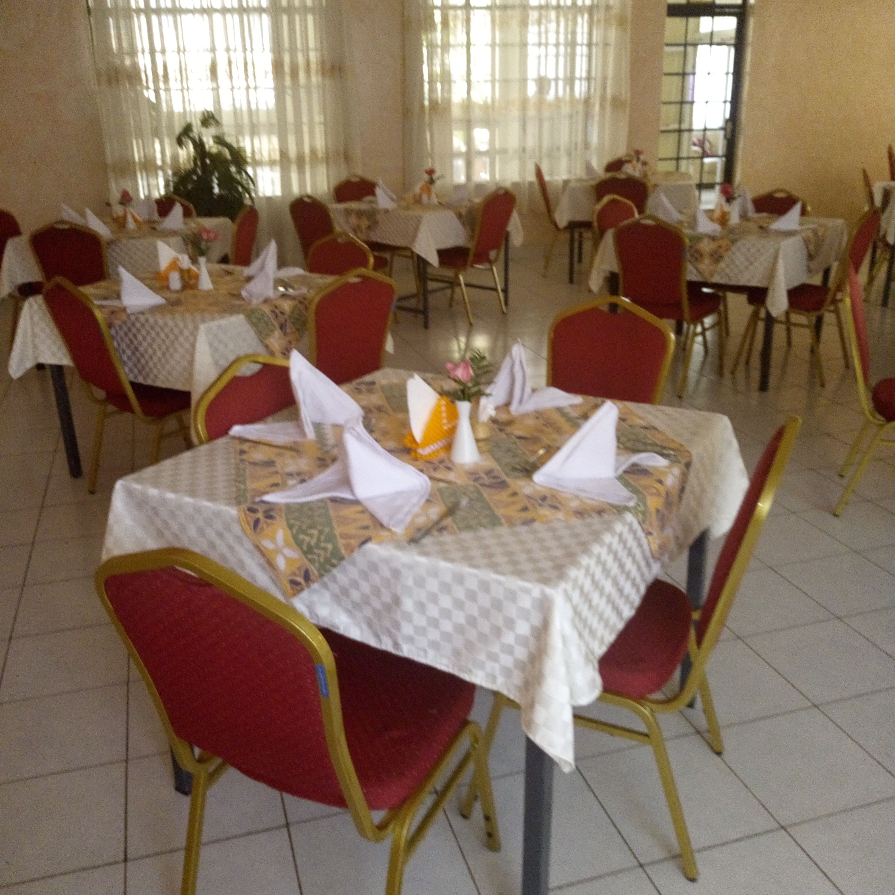 Comedor con mesas dispuestas para varios comensales, sillas rojas y manteles blancos.