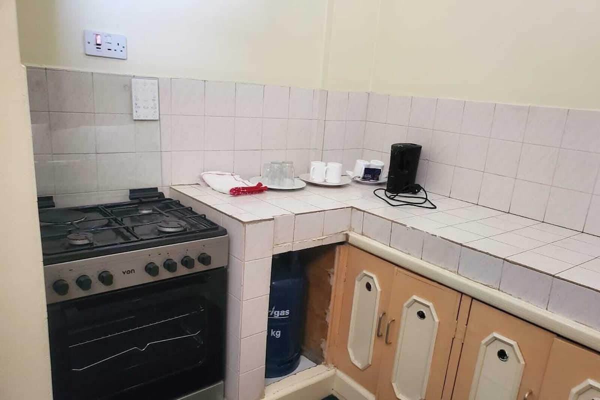 A compact kitchen with a gas stove, oven, and a small countertop with a coffee maker and cups.