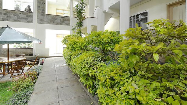 A spacious indoor courtyard with a tiled floor, a wooden table and chairs, and a variety of green plants. - LMS Guest House (Nairobi)