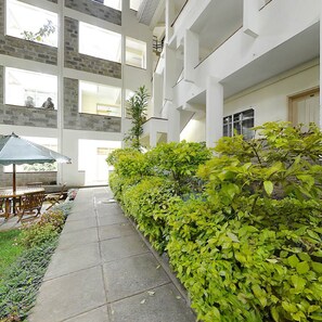 A spacious indoor courtyard with a tiled floor, a wooden table and chairs, and a variety of green plants. - LMS Guest House (Nairobi)