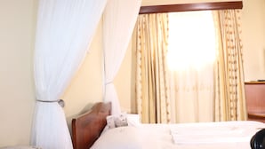 A hotel room with a bed, curtains, and a window with floral curtains. - LMS Guest House (Nairobi)