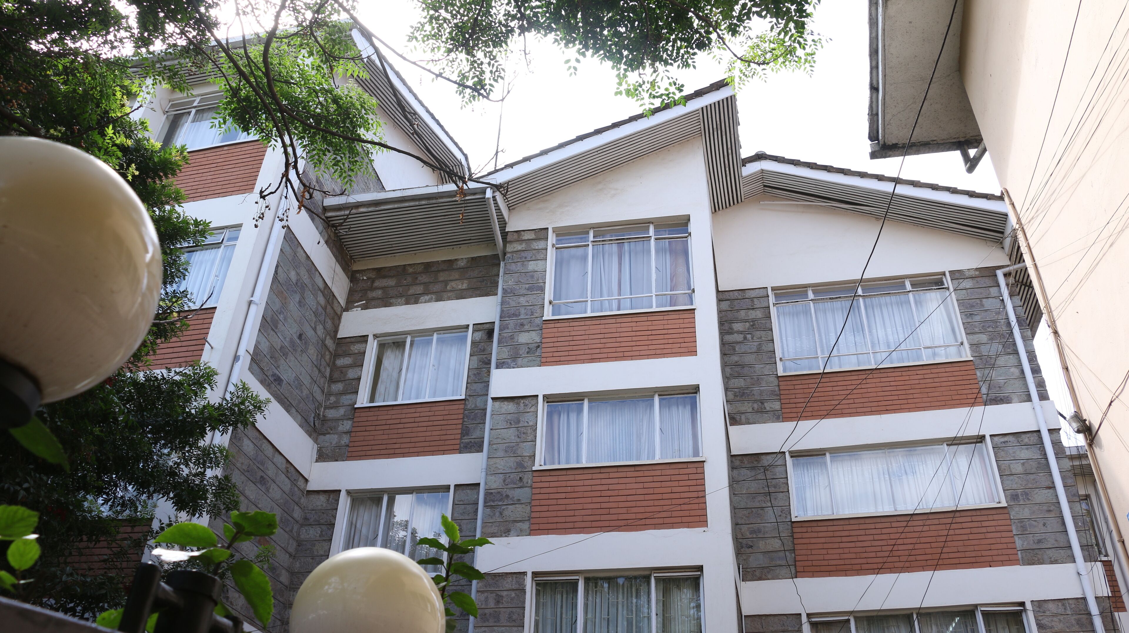 A multi-story building with a modern architectural design, featuring a combination of brick and stone facades, large windows with white curtains, and visible electrical wiring.