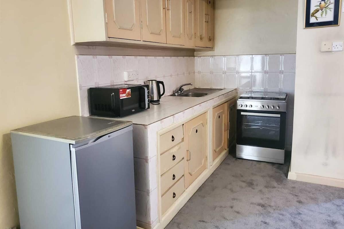 A compact kitchen with a refrigerator, microwave, kettle, sink, and stove.