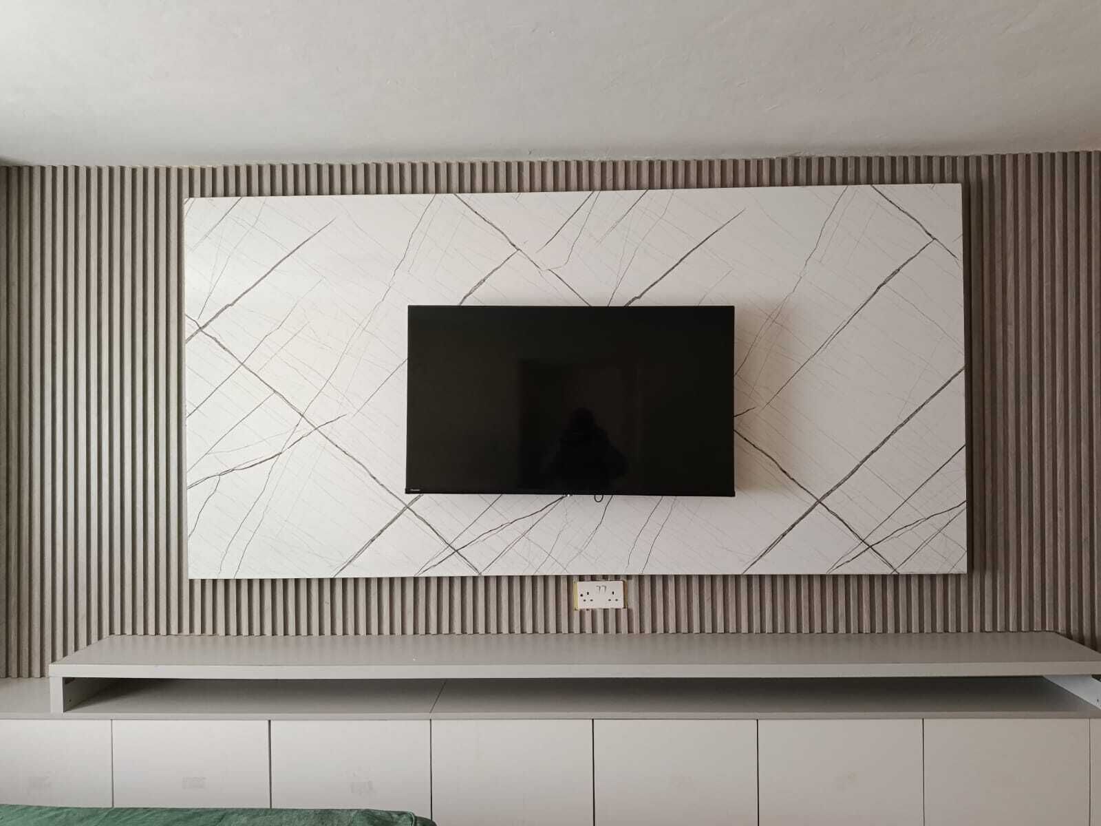 A modern wall-mounted TV with a geometric pattern, a power outlet, and a built-in shelf below.