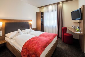 Hotellihuone, jossa on suuri sänky, seinälle asennettu televisio, työpöytä tuolilla ja vaatekaappi.