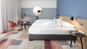 A modern hotel room with a large bed, a round mirror, a red chair, a small table, and a blue wall. - Hotel Schwanen Köngen (Kongen)