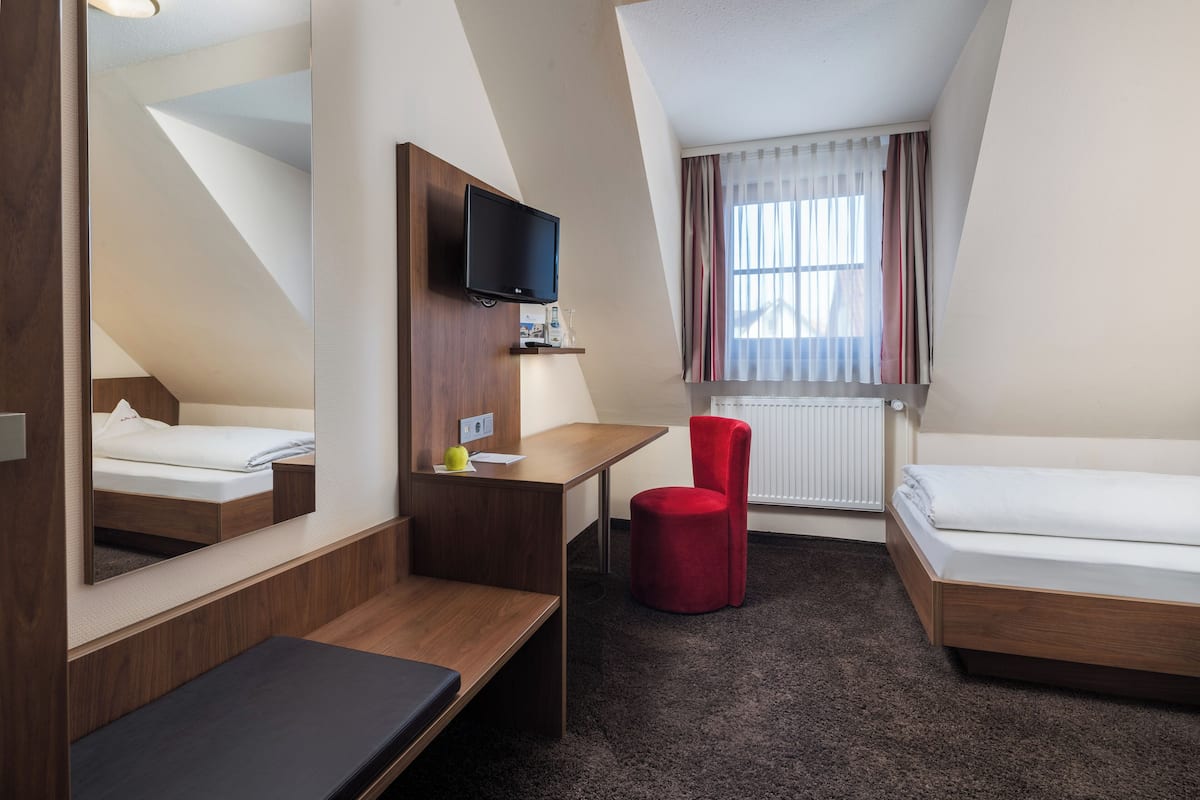 A hotel room with a bed, a desk, a chair, a TV, and a window with curtains.