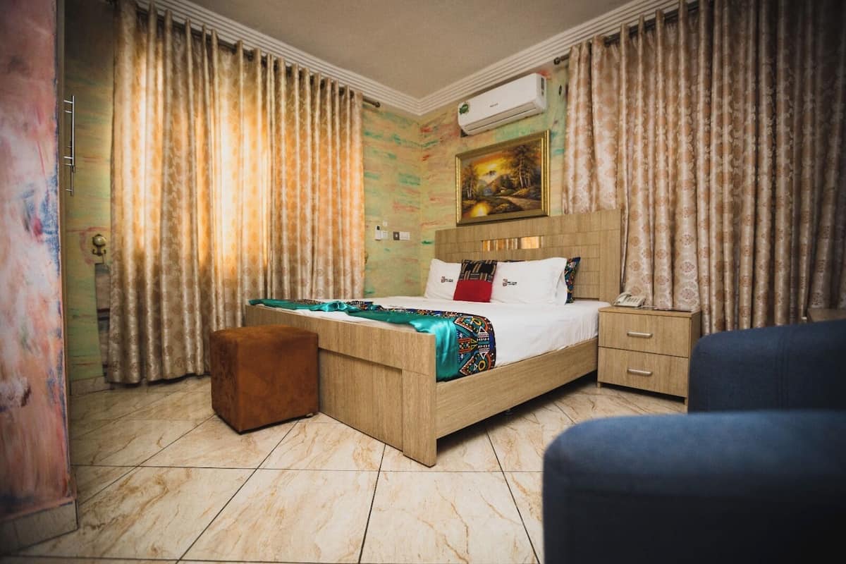 Una habitación de hotel con una cama, una mesita de noche, una silla y un cuadro en la pared.