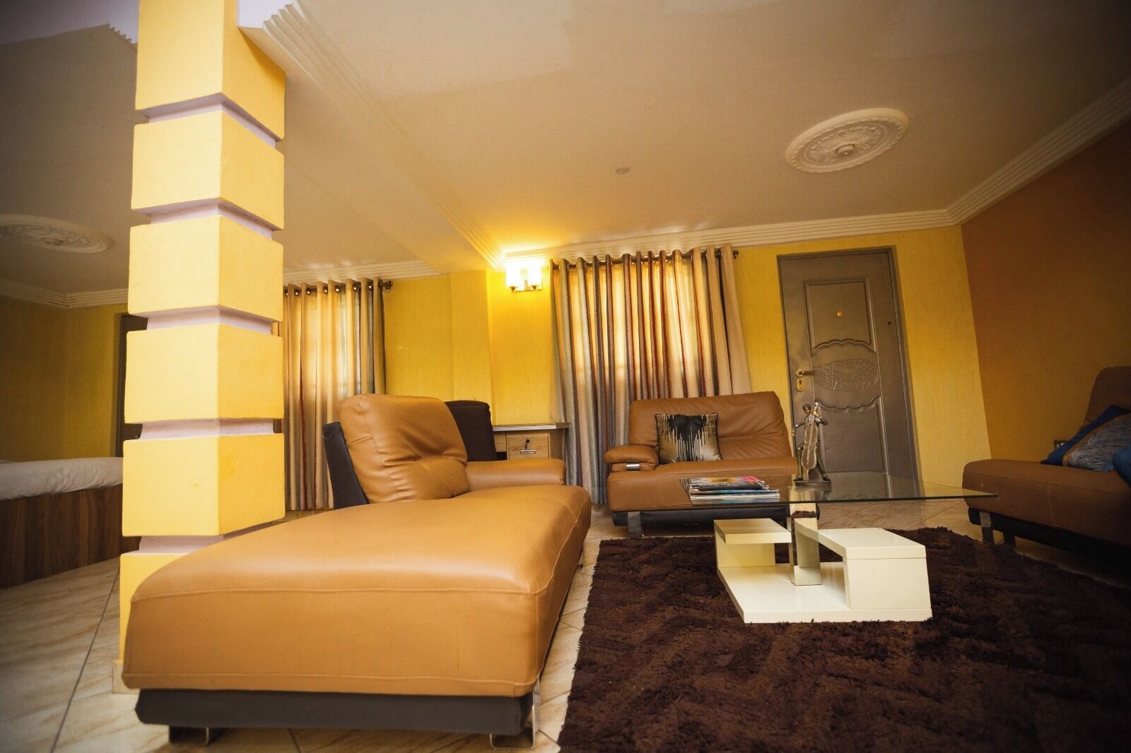 A hotel room with a large bed, two armchairs, a sofa, a glass coffee table, and a door with a decorative handle.