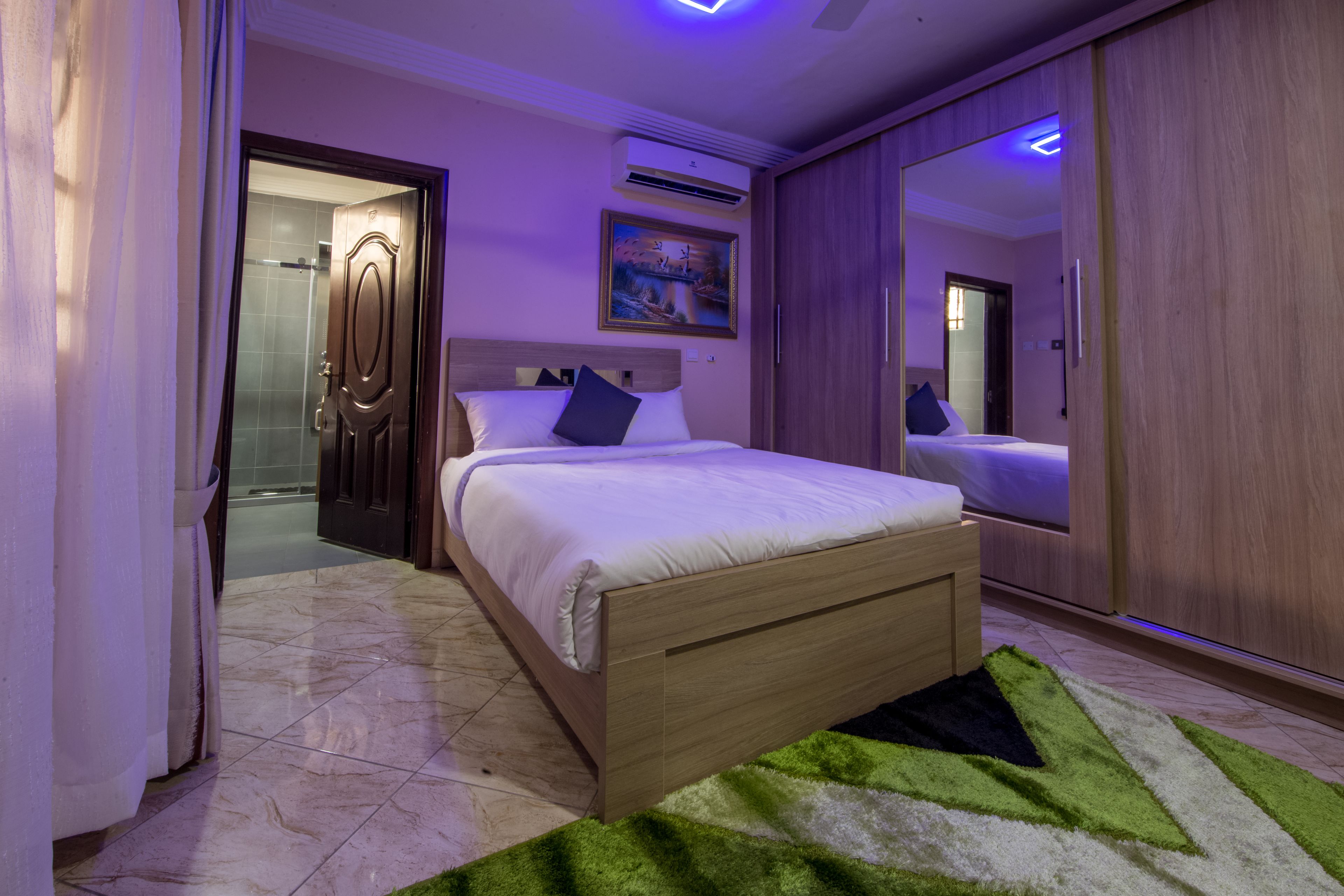 Un dormitorio con cama, espejo, puerta y un cuadro en la pared.