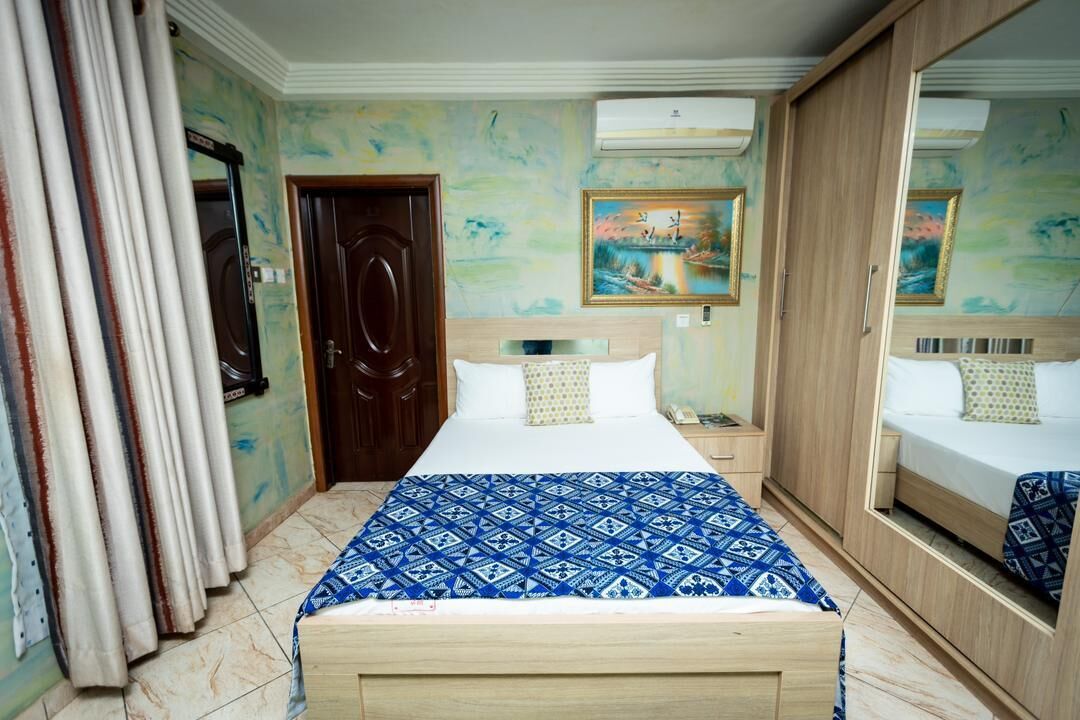 A bedroom with a bed, a nightstand, a wardrobe, a door, and a painting on the wall.