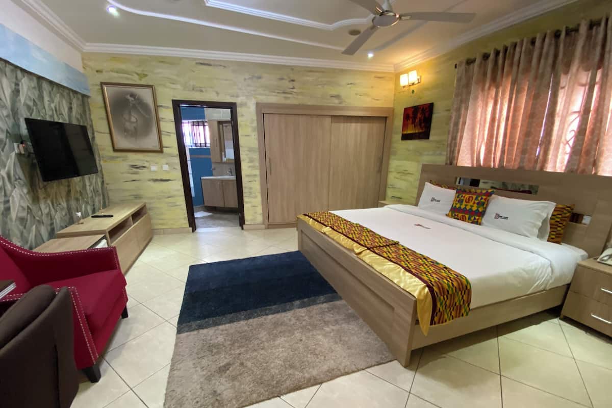 Habitación de hotel con una cama, un escritorio, una silla, un televisor y un baño visible a través de una puerta abierta.