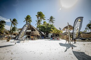 A beachside property with flags, a thatched-roof structure, and palm trees. - KiteActive Guesthouse (Paje)
