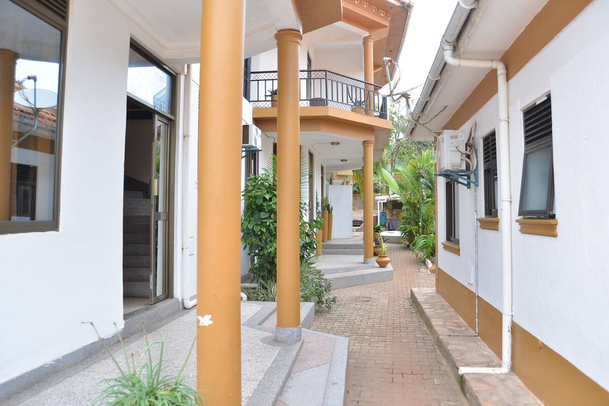 A corridor with a tiled floor, columns, and potted plants.