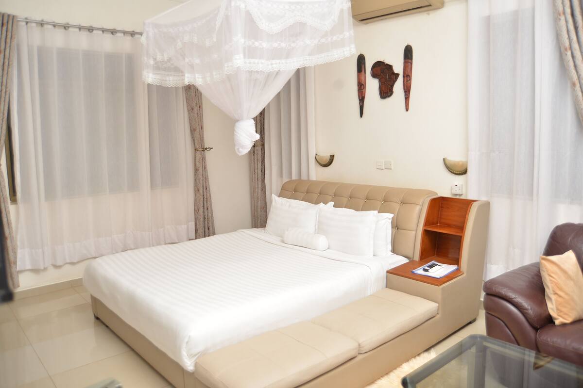 A bedroom with a large bed, a bedside table, a leather armchair, and a glass coffee table.