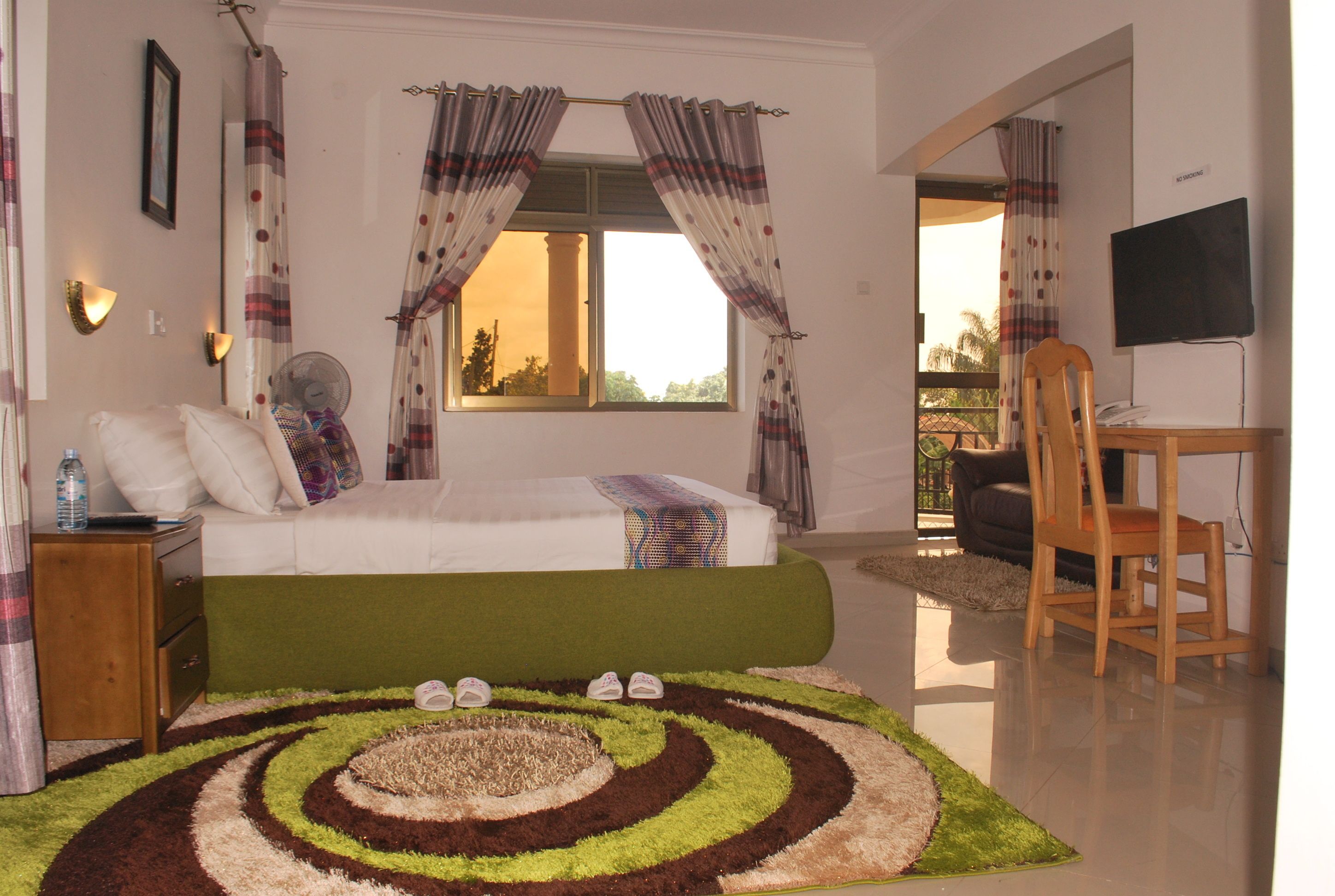 A bedroom with a bed, a desk, a chair, a fan, and a view of the outdoors.