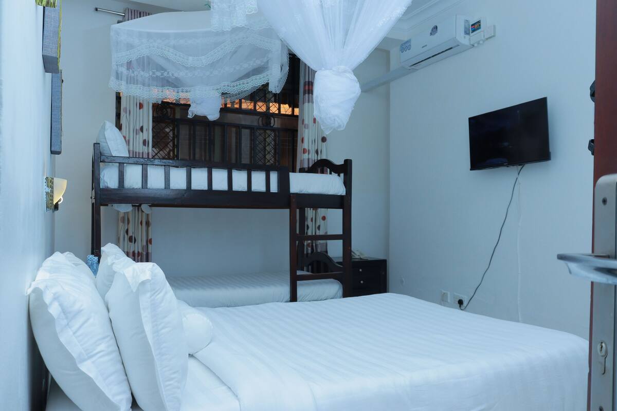 A room with bunk beds, a television mounted on the wall, and a mosquito net above the upper bunk.