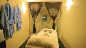 Relax in this serene hotel room featuring a single bed, glass shower enclosure, and a small mirror above the bed.